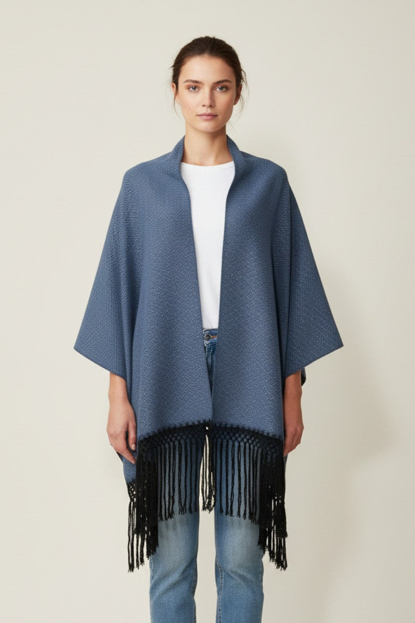 Woman wearing a blue handwoven cotton shawl with black fringe, styled as a poncho on a neutral background