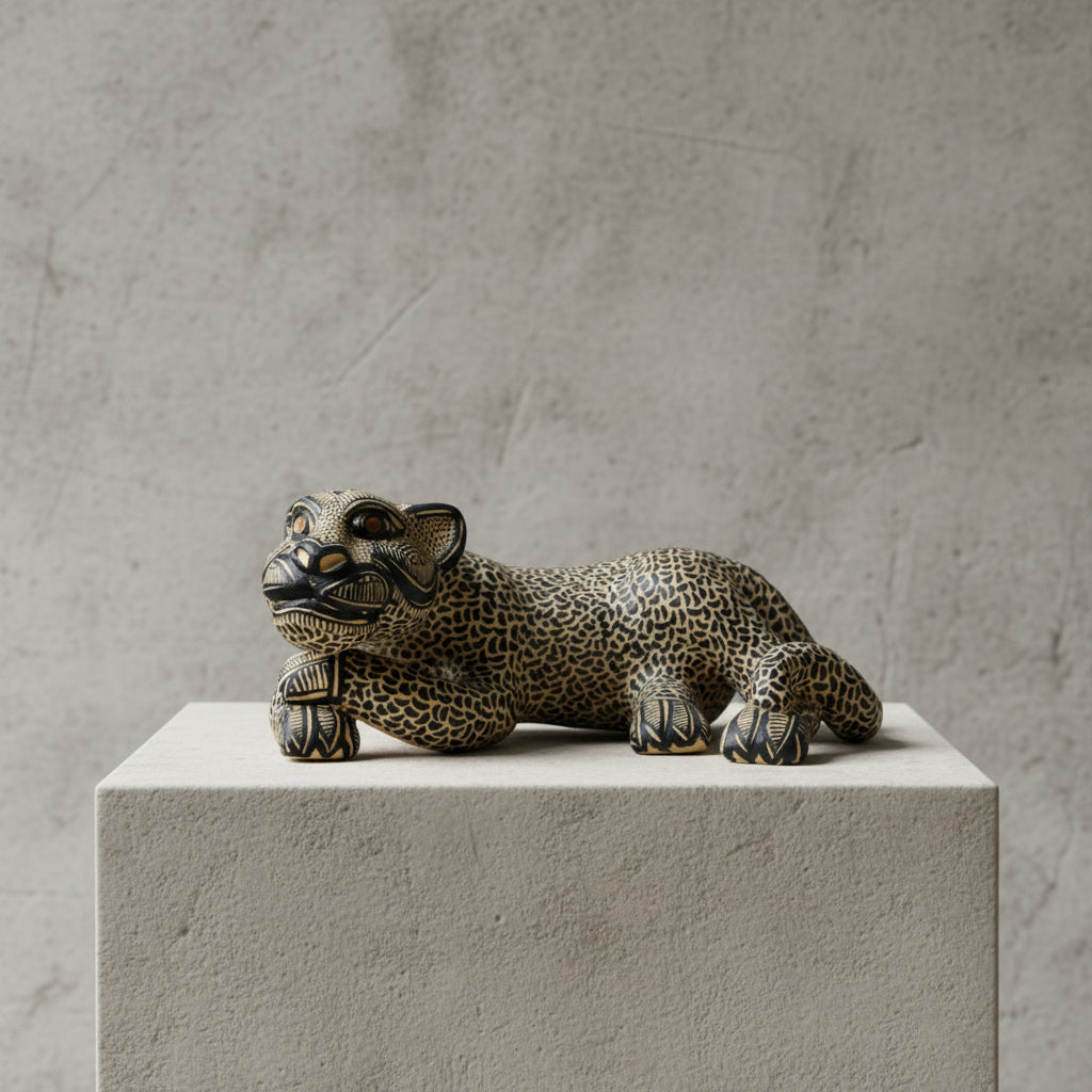 Handmade Mayan clay jaguar sculpture with gold and black details, shown on a concrete block against a neutral gray wall