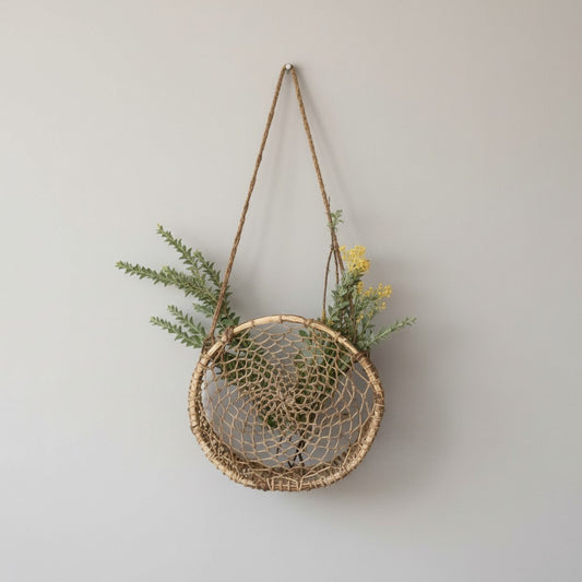 Woven circular jonote wall hanging basket with greenery against a neutral wall.