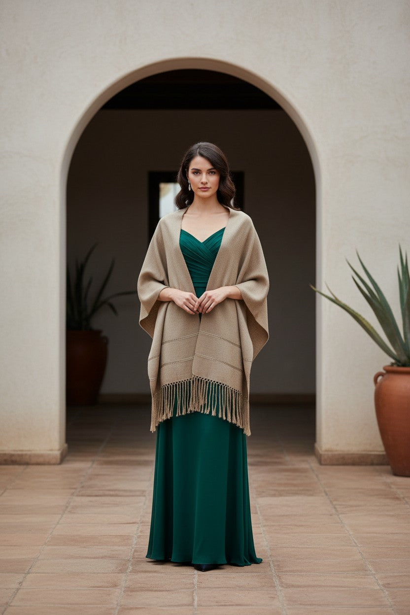 Woman wearing a taupe handwoven rebozo shawl over an emerald green formal dress, standing under an arched entryway
