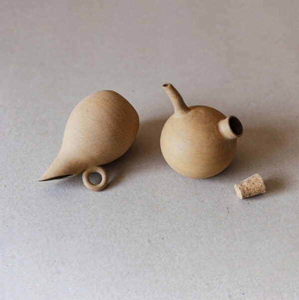 Handmade ceramic oil and vinegar cruets lying on their sides, showing the pointed spouts, loop handle, and cork stopper detail