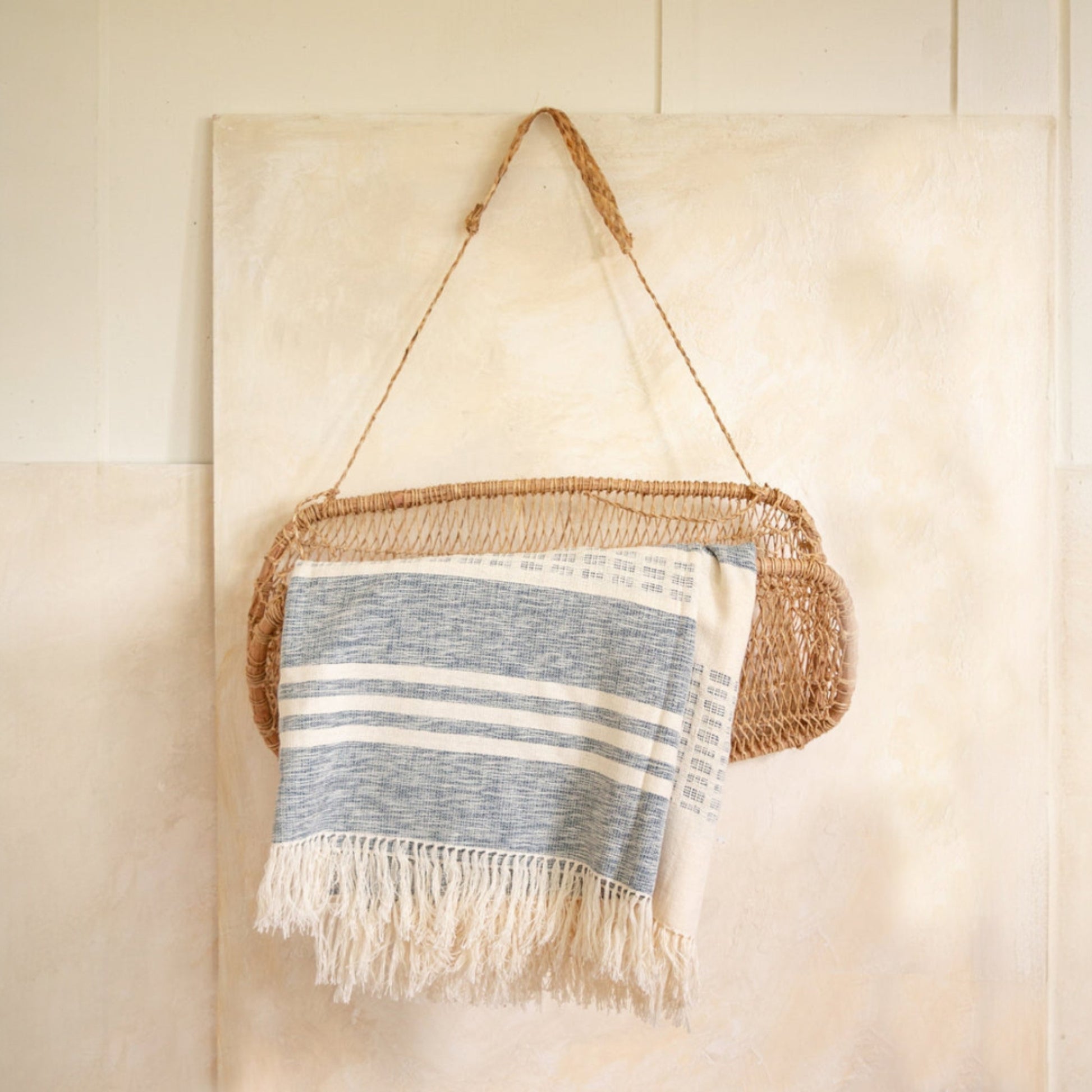Jonote wall basket hanging on a tiled wall, holding a folded striped textile.